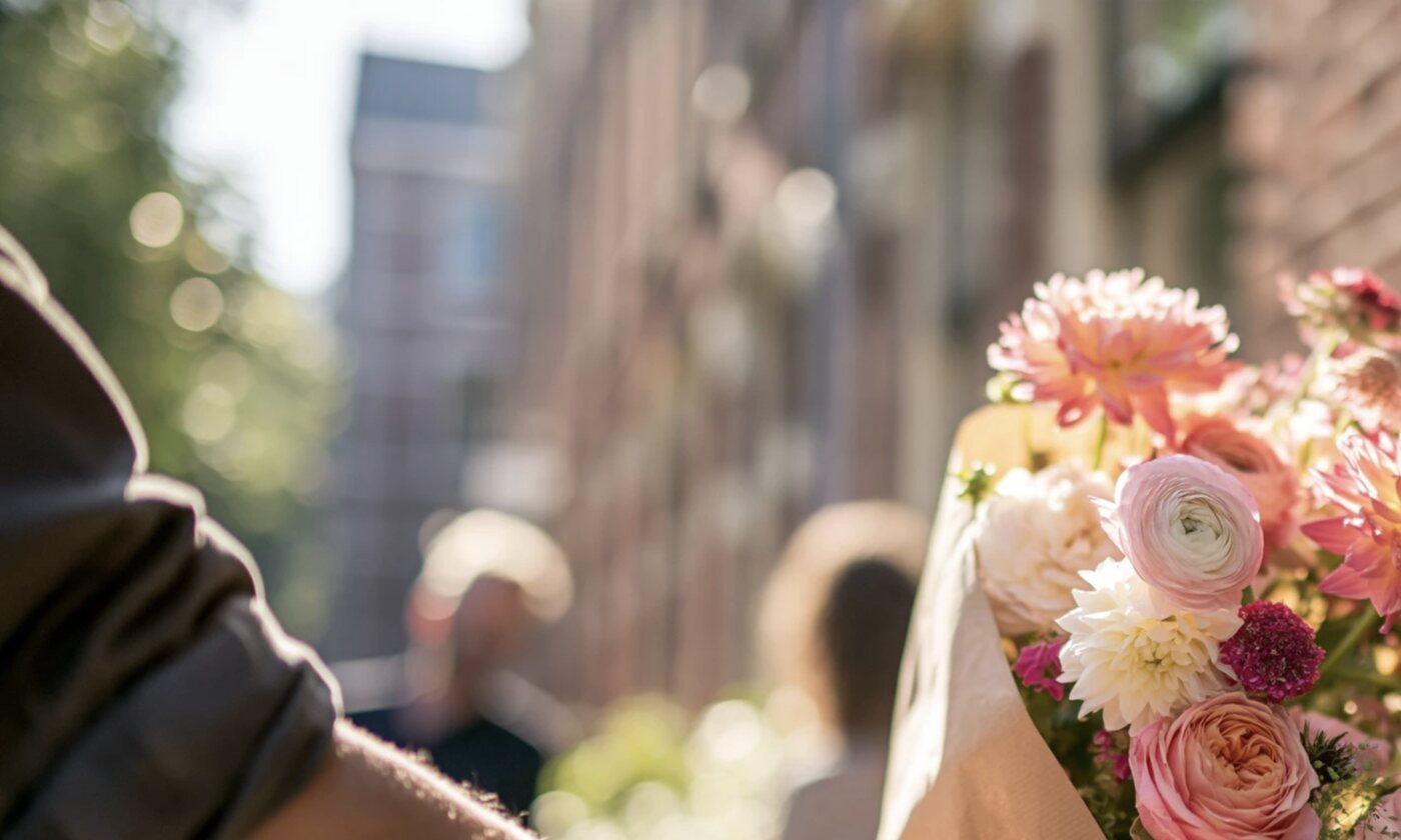 Een vrouw neemt bij haar voordeur een boeket aan, de bloemen scherp in het ochtendlicht